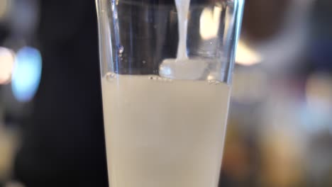 Pouring-alcoholic-cocktail-into-glass-with-ice-cubes-on-bar-counter,-close-up