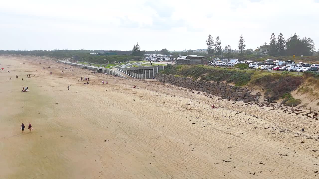 Aerial footage captures Ocean Grove beach, showcasing sandy shores, coastal vegetation, and nearby parking under soft daylight