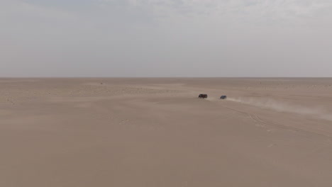 two cars driving through the desert toward bar al hikman, oman, aerial view
