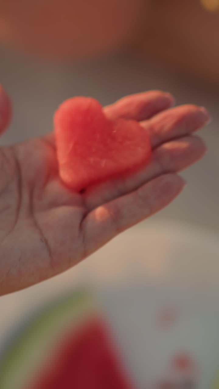 primer plano de la mano sosteniendo una rebanada de sandía en forma de corazón, que simboliza el amor y la frescura, con una delicada pulsera que mejora la elegancia en la cálida luz exterior