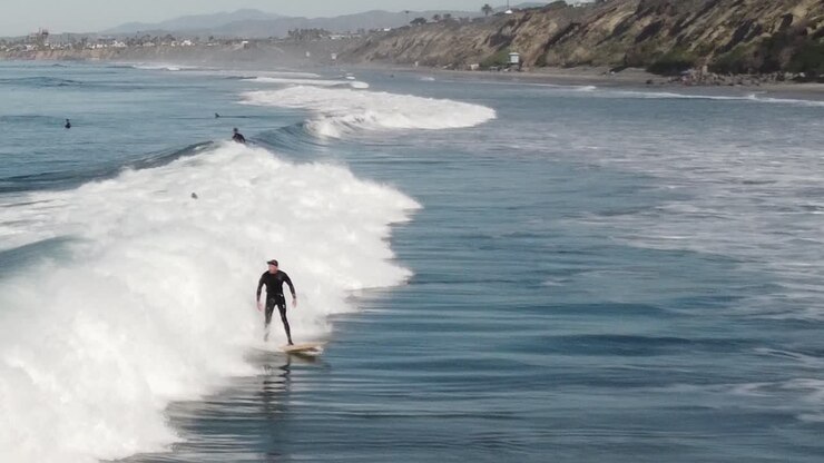 A beautiful aerial drone shot of surfers surfing a wave close to the beach, Carlsbad State Beach - California