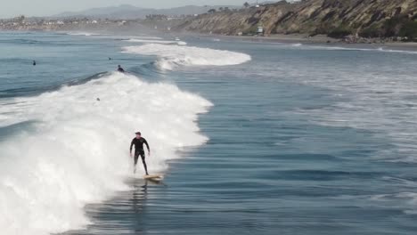 A-beautiful-aerial-drone-shot-of-surfers-surfing-a-wave-close-to-the-beach,-Carlsbad-State-Beach---California