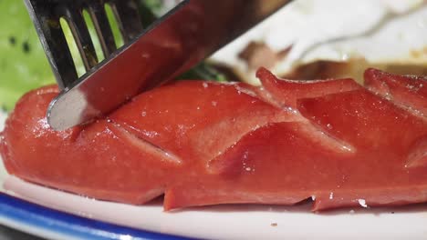 close-up of cutting a grilled sausage with a fork and knife on a plate
