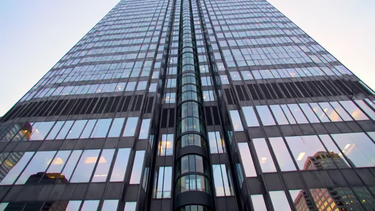 A towering glass building reflects the vibrant hues of sunset, showcasing contemporary architecture amidst a busy urban landscape. Observers admire the structure's impressive design.