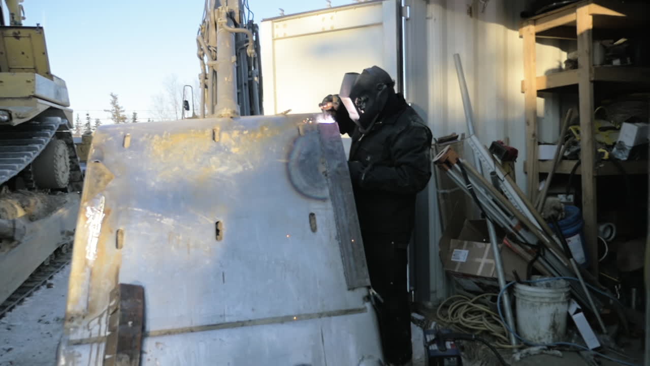 Slow-Motion of Man Welding on a excavator in a rural Alaskan Village in winter.