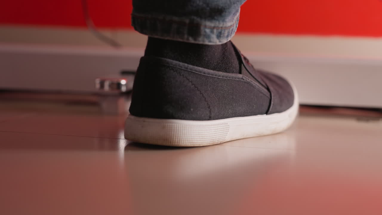 검은 신발과 파란 청바지를 입은 발은 부드럽고 반사적인 바닥을 부드럽게 니다. 배경에는 부드러운 은 색조가 있으며, 장면에 따뜻함과 대조를 더합니다.