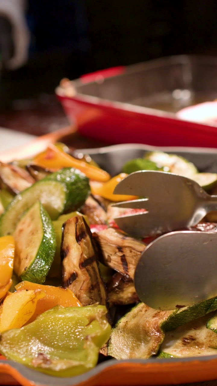 Pinze metalliche prendono zucchine e peperoni arrostiti da un vassoio da buffet all'interno