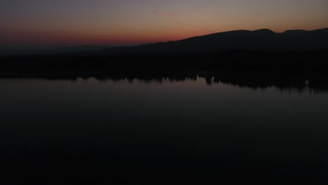 Tilt-up-shot-of-sunrise-or-sunset-view-with-reflection-on-the-water-and-mountains-in-the-background