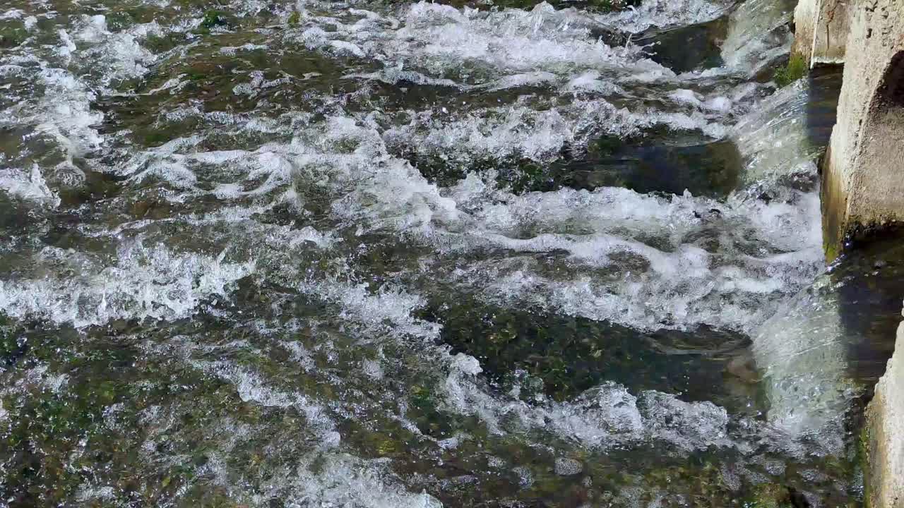 Closeup of dynamic fast flowing water stream, ripples and currents in crystal clarity, comes under dirt road.