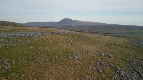 Moorland-rocky-hillside-rise-up-revealing-mountain-Ingleborough-on-horizon-in-English-countryside-Yorkshire-UK