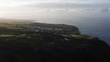 Drone-footage-of-subtropical-volcanic-island-countryside-at-sunset-with-homes-near-ocean-cliff-on-the-Azores-Sao-Miguel-Island