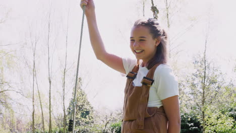 Portrait-Of-Girl-Having-Fun-On-Tyre-Swing-In-Garden-At-Home