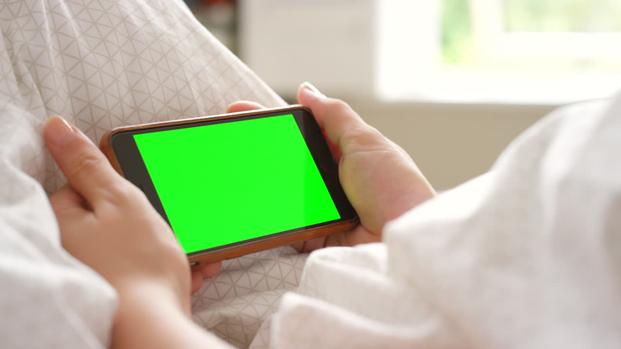 침대에서 녹색 화면을 가진 스마트폰을 들고 있는 사람
