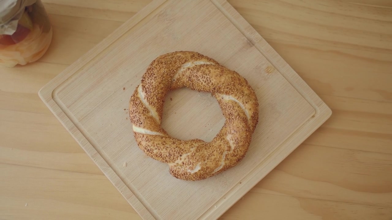 Hand Picking Up a Fresh Sesame Simit from a Wooden Board