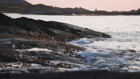 Waves-slowly-crash-onto-the-rocky-shore-lit-by-the-setting-sun