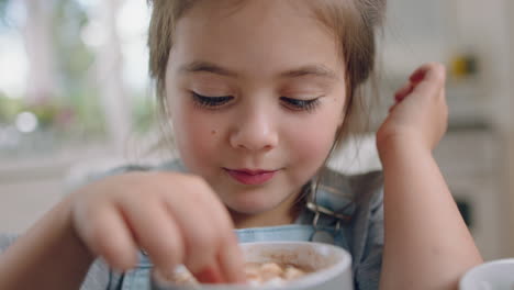 cute little girl eating cookie dipping biscuit into hot chocolate enjoying delicious treat at home in kitchen