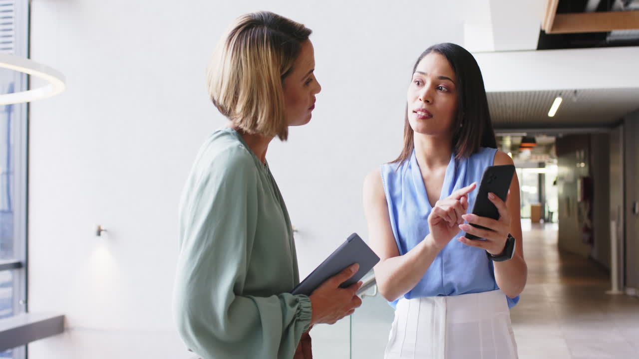 Discussing project details, businesswomen in office using smartphone and holding tablet