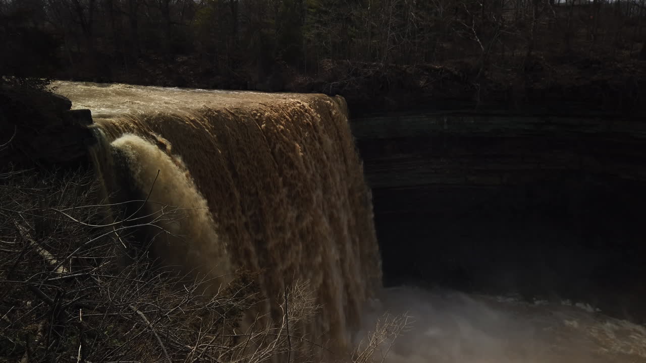 Wide shot of a swift current dropping over Balls Falls with tilt down to the misty river below