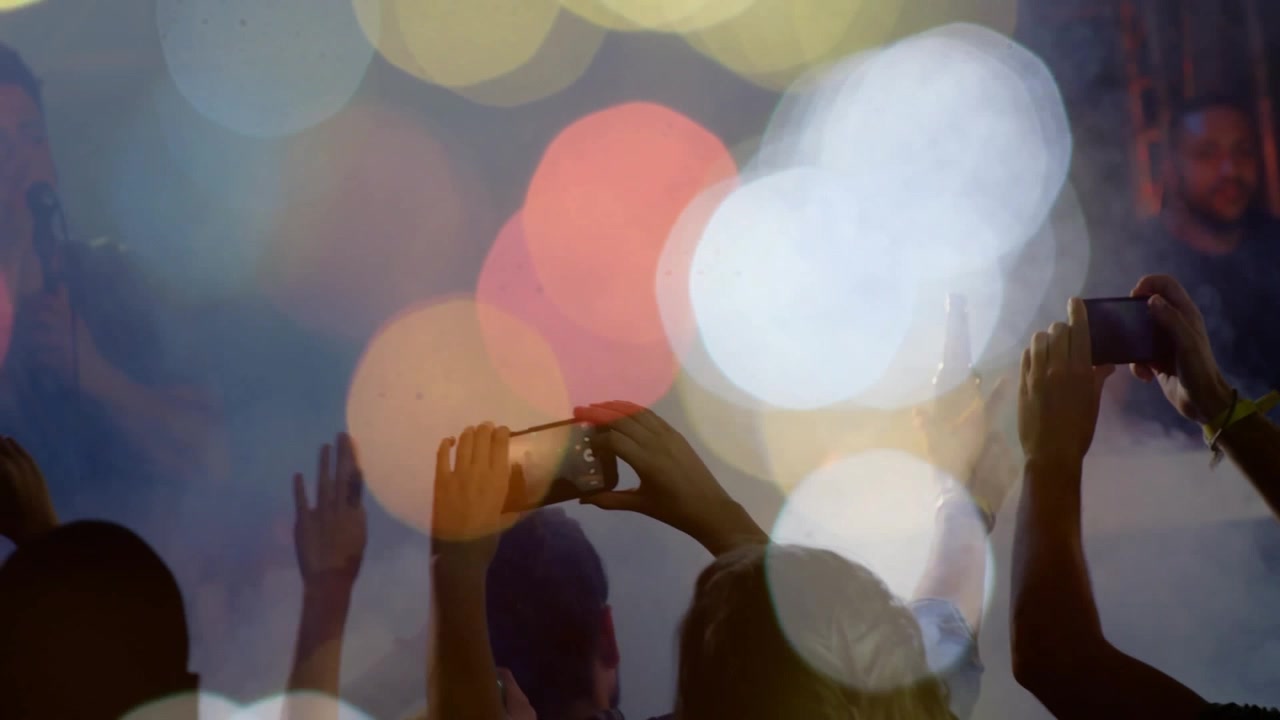 Publikum løfter smartphones, vinker på et dunkelt spillested med bokeh-lys og filmer sangeren.