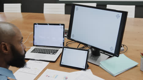 African-american-businessman-using-computer,-tablet-and-laptop,-copy-space-on-screens,-slow-motion