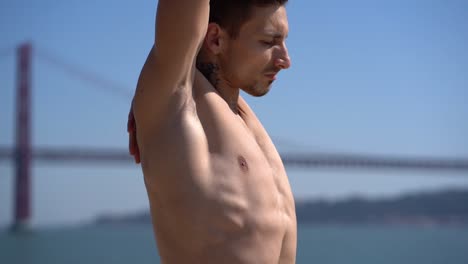 muscular shirtless sportsman stretching at riverside