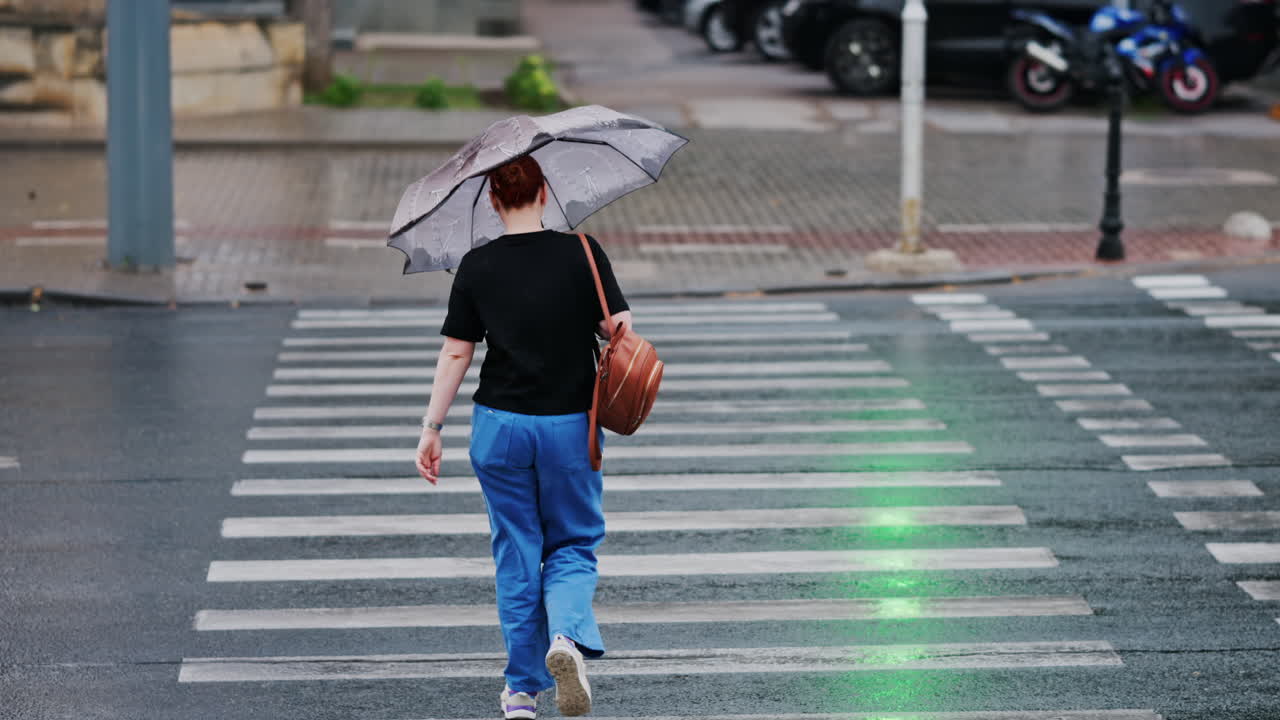 Woman holding an umbrella crossing the street at a green light on a rainy day in Chisinau, Moldova