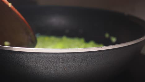close-up of green food being stirred in a frying pan