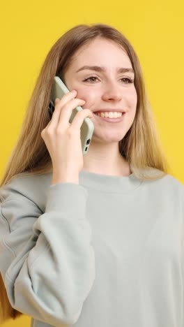 young woman talking on mobile phone on yellow background