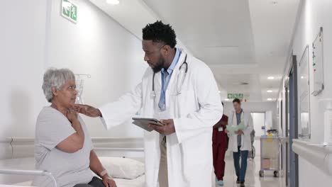 Diverse-serious-male-doctor-with-tablet-talking-to-senior-patient-on-bed-in-slow-motion,-unaltered