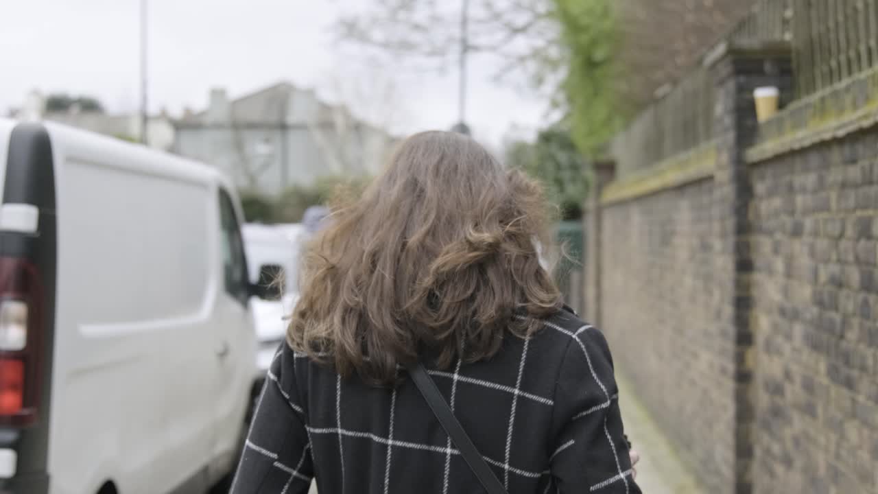 vista trasera de una mujer de negocios con el pelo largo y castaño caminando por una calle concurrida mientras el viento le sopla el pelo en el centro de londres