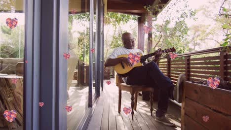 Animation-Von-Rosa-Blumen-über-Einem-älteren-Afroamerikanischen-Mann,-Der-Auf-Der-Heimischen-Terrasse-Gitarre-Spielt