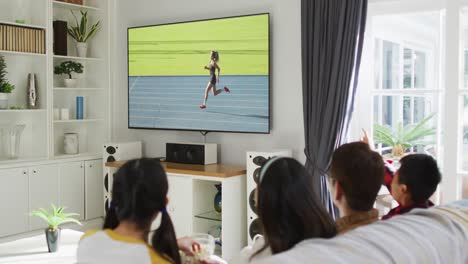 Compuesto-De-Familia-Feliz-Sentados-Juntos-En-Casa-Viendo-Atletismo-Corriendo-En-La-Televisión