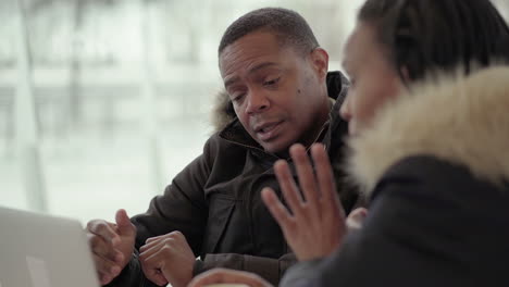 afro-american middle-aged man in black jacket with fur hood disagreeing with afro-american young girl with braids drinking coffee outside