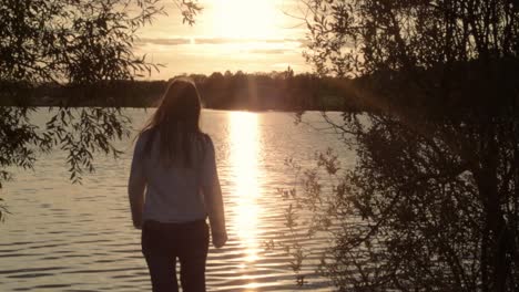 Frauensilhouette,-Die-Bei-Sonnenuntergang-Auf-Den-Plätschernden-See-Zugeht