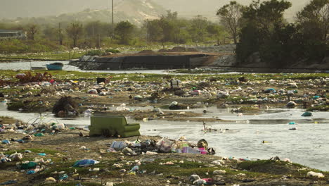 winding river banks covered in plastic garbage piles in vietnam, static view