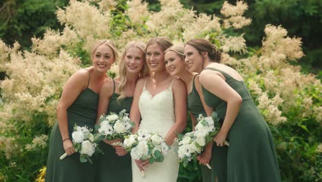 bride and bridesmaids leaning in together with bouquets in garden slow motion