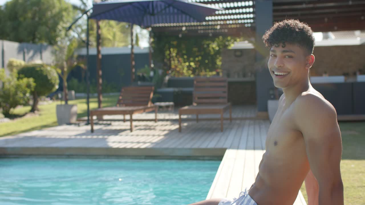 African American man in trunks noticing camera, turning from recline to smiling at pool, copy space