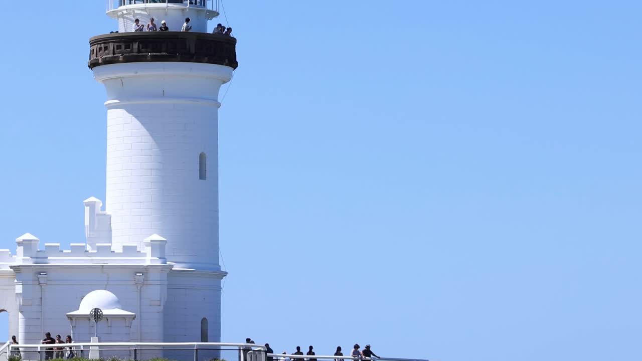 Detailed view of a white lighthouse tower with visitors on a clear, sunny day.