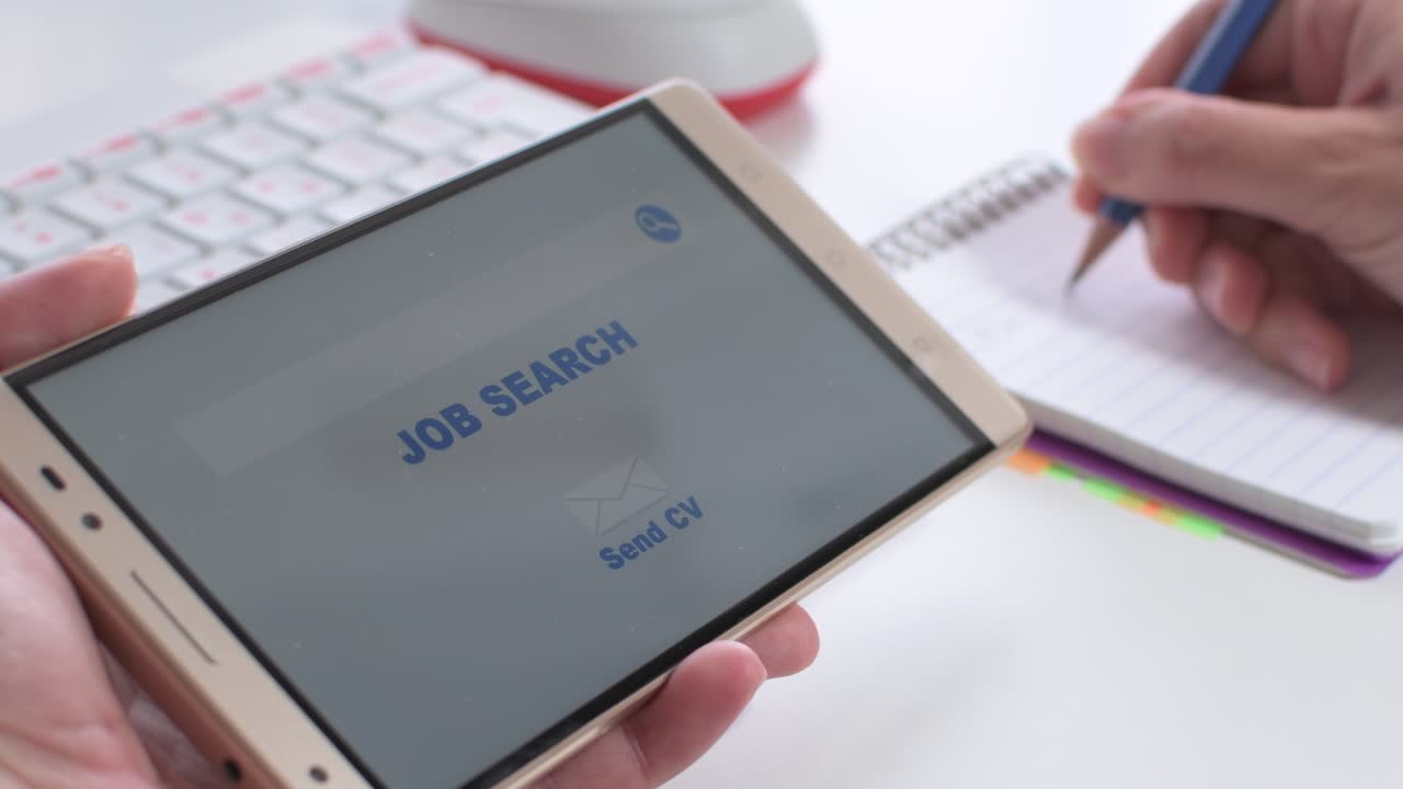 Online job search, woman's hands holding a mobile in which an employment website appears, and taking notes in a notebook.