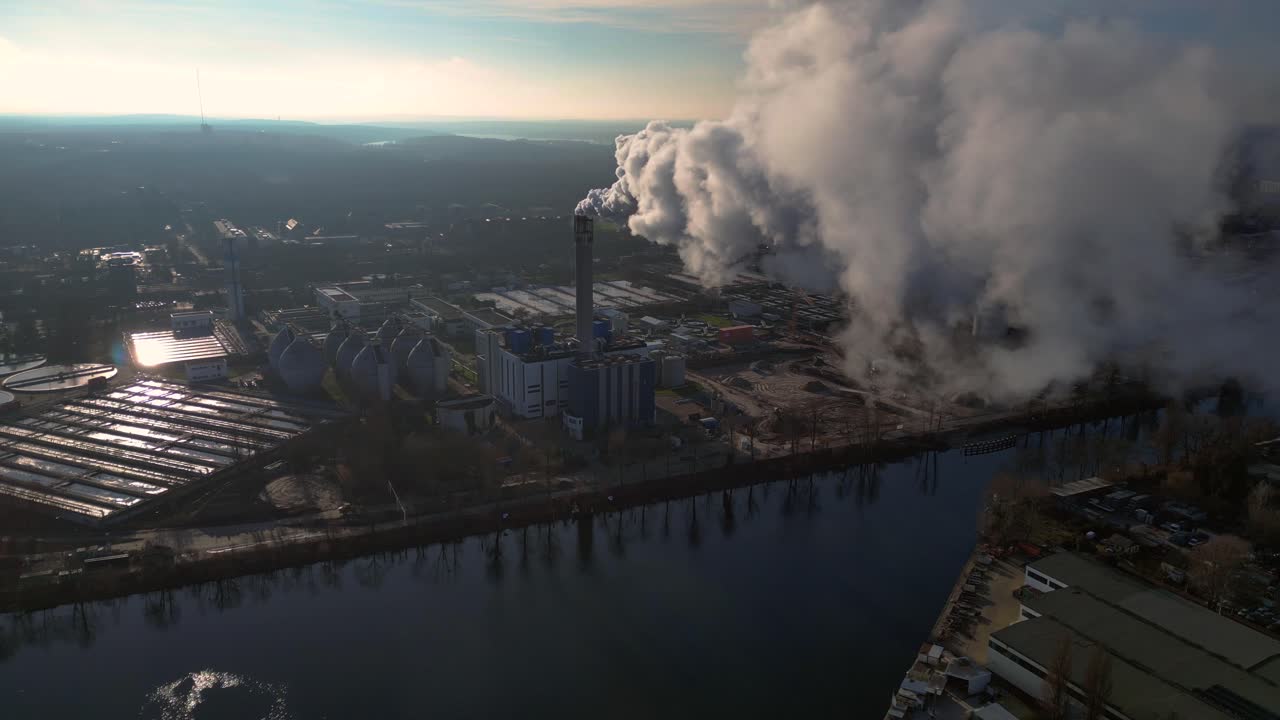 Industrial chimneys emitting white smoke over city skyline under blue sky, concept of pollution. Dramatic aerial view flight drone top down Above view