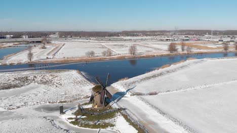 Dutch-people-ice-skating-beside-windmill-on-frozen-canals,-winter-aerial-view