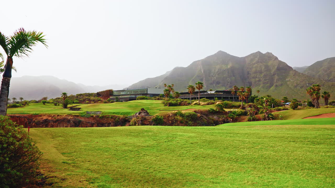 해안선 근처에 있는 테네리페에 있는 골프 코스의 파노라마 뷰. 뒷면에는 초록색, 나무, 초록색 산이 보인다.