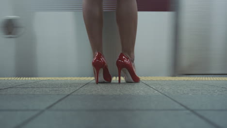 a woman in red heels waits for a subway train