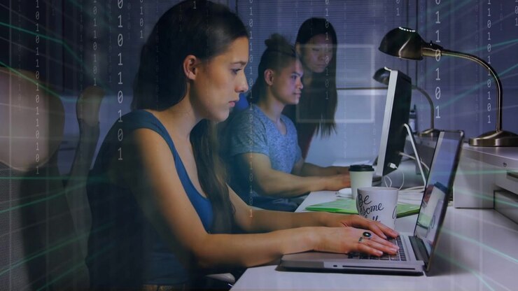 Front woman typing while team watching monitors, binary overlay rising as typing, aiding tech work