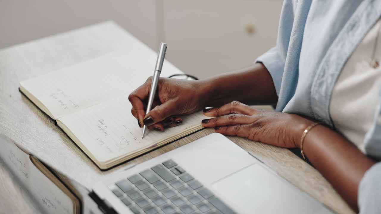 Woman writing in notebook with laptop