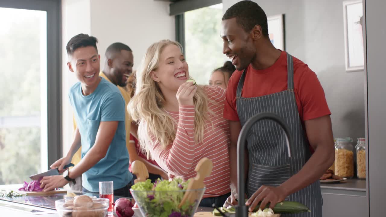 Happy diverse group of friends preapring meal in kitchen, slow motion