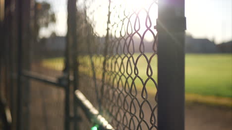 a chain link fence gate with locks on it at sunrise outside of a grass baseball field in a public park