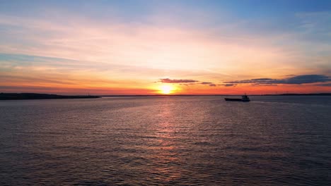 A-serene-barge-drifts-beneath-Humber-Bridge,-a-tranquil-scene-unveiled-in-aerial-drone-footage-during-the-golden-sunset