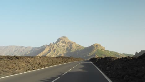 Driving-on-a-highway-with-piles-of-stones-along-the-roadside-going-towards-the-mountain-during-sunset,-pov