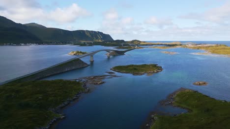 flying along fredvang bridge in lofoten northern norway with the sea ocean water shimmering in light turquoise blue and green tones on a sunny day in summer with little islands surrounding the road